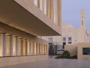 Sand brick building of Assila Investment HQ in Riad with louvers and Moschee in background.